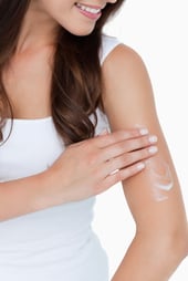Smiling brunette applying some cream on her arm against a white background